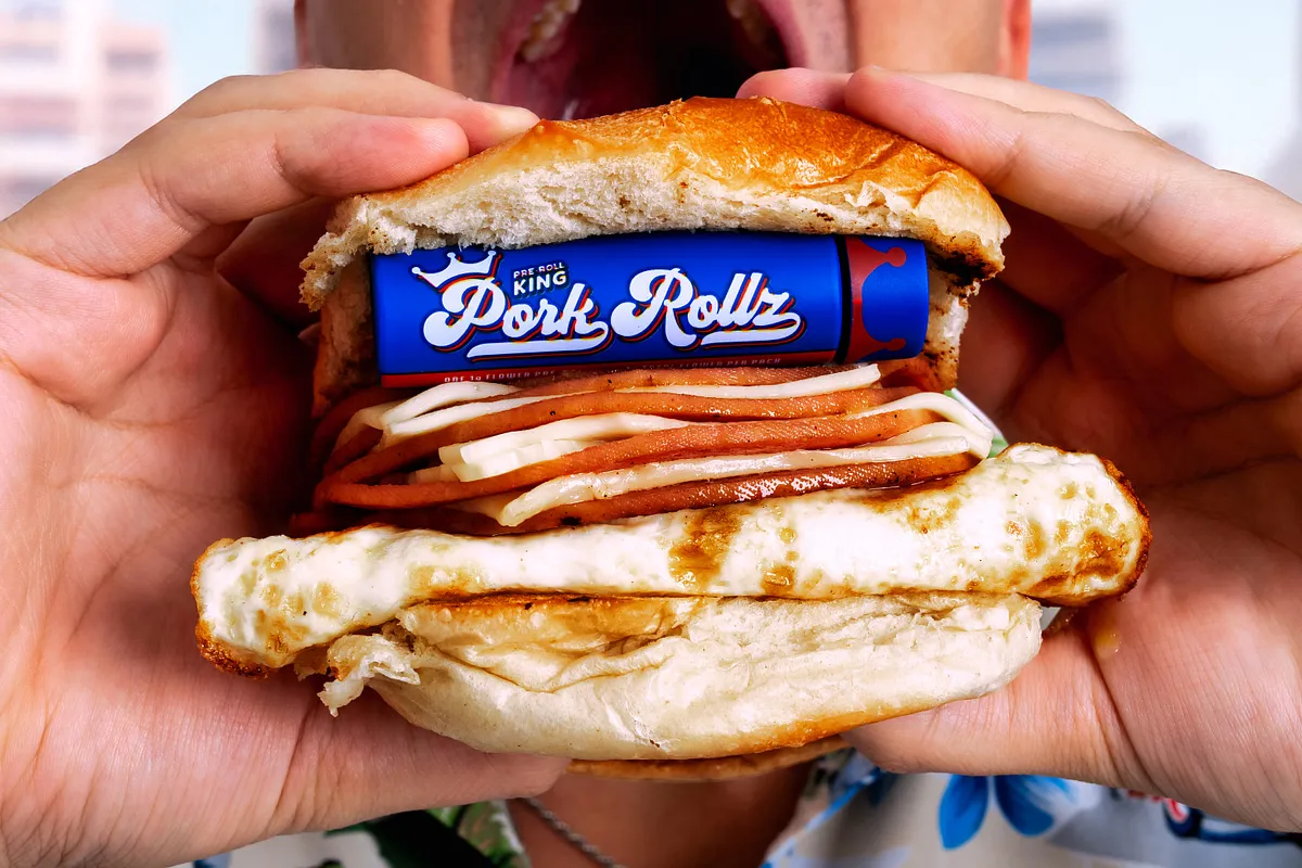 Hands holding a pork roll, egg and cheese sandwich with a Pork Rollz pack tucked inside the bun