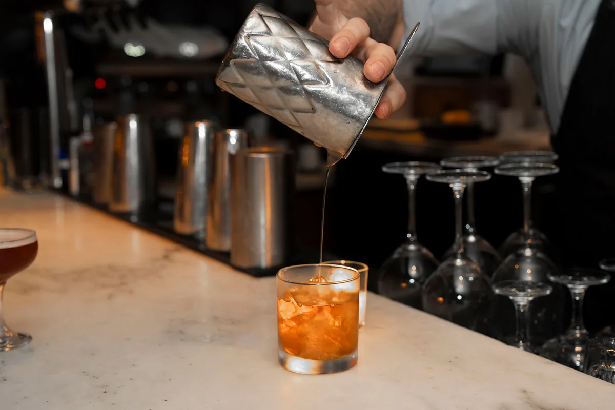 Bartender straining a cocktail into a glass at the bar