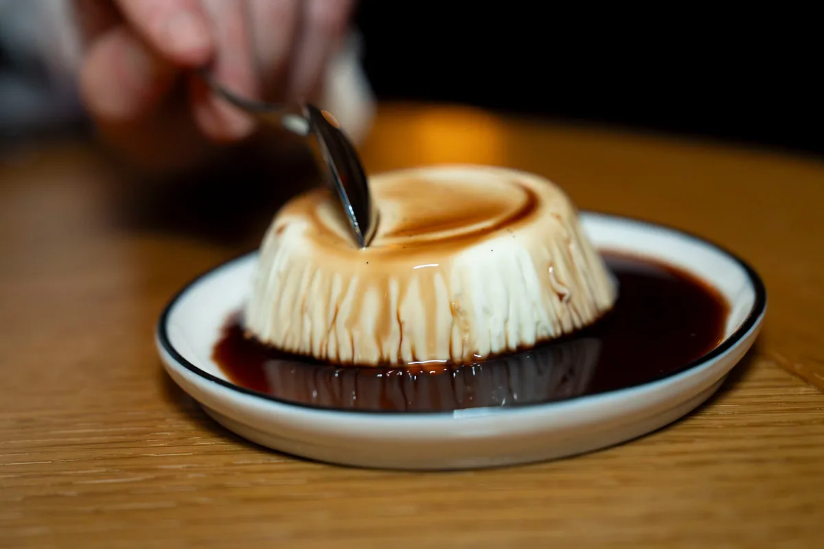 Spoon breaking into a set custard dessert in caramel