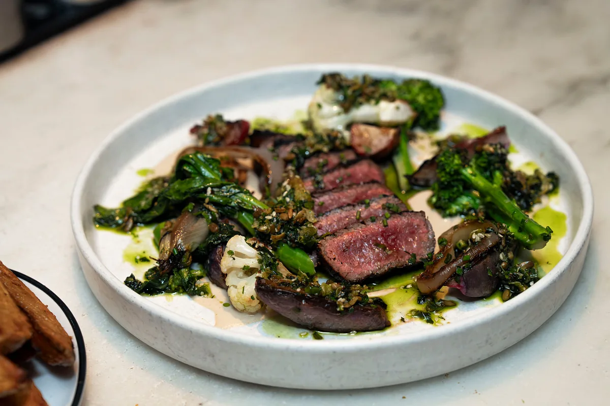 Sliced steak plated with mushrooms, broccolini and herb oil