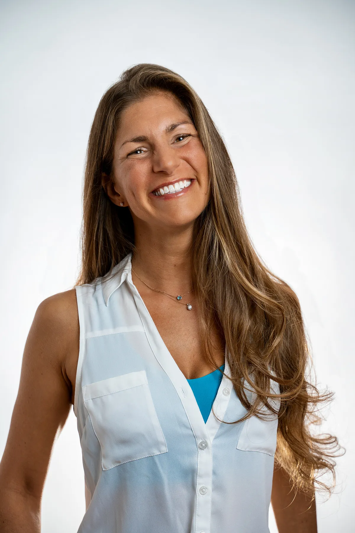 Laughing woman with long hair in a white sleeveless blouse against a white studio backdrop