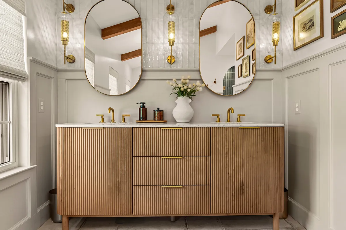 Fluted wood double vanity beneath arched mirrors and brass sconces