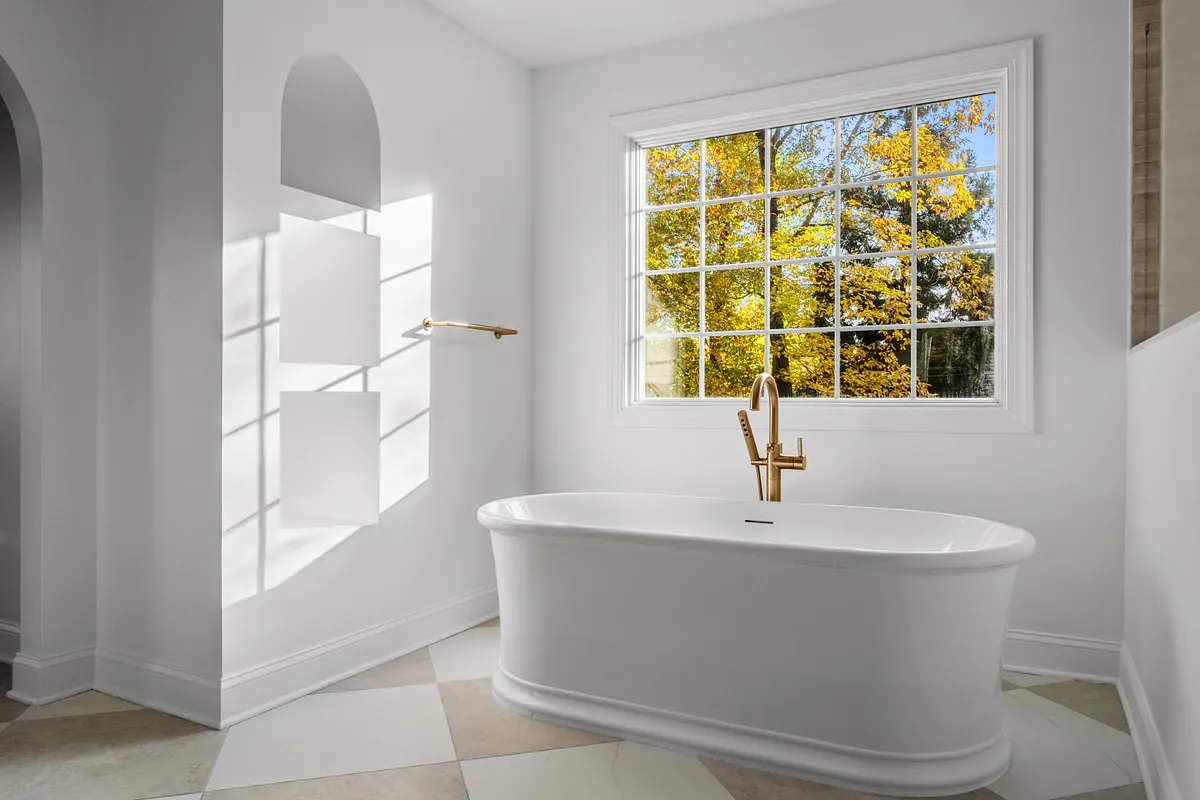 Freestanding tub beneath a gridded window beside an arched wall niche
