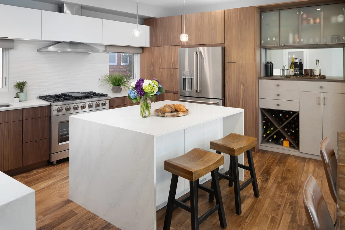Kitchen with a white waterfall island, wooden stools and walnut cabinetry