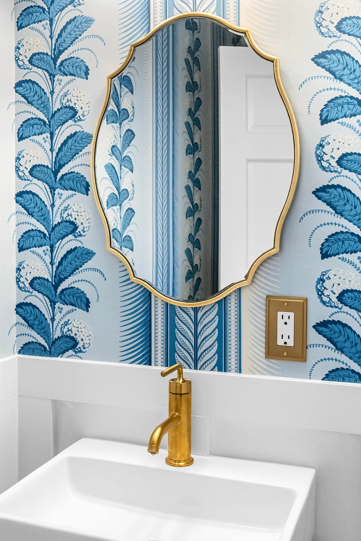 Powder room with blue botanical wallpaper, a scalloped brass mirror and brass tap