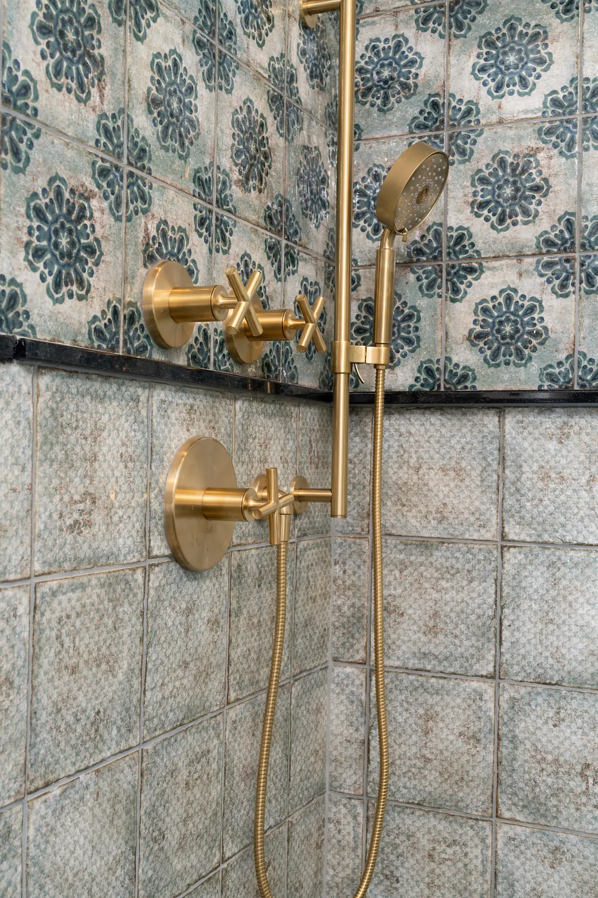 Brushed brass shower valves and handheld shower on patterned blue tile