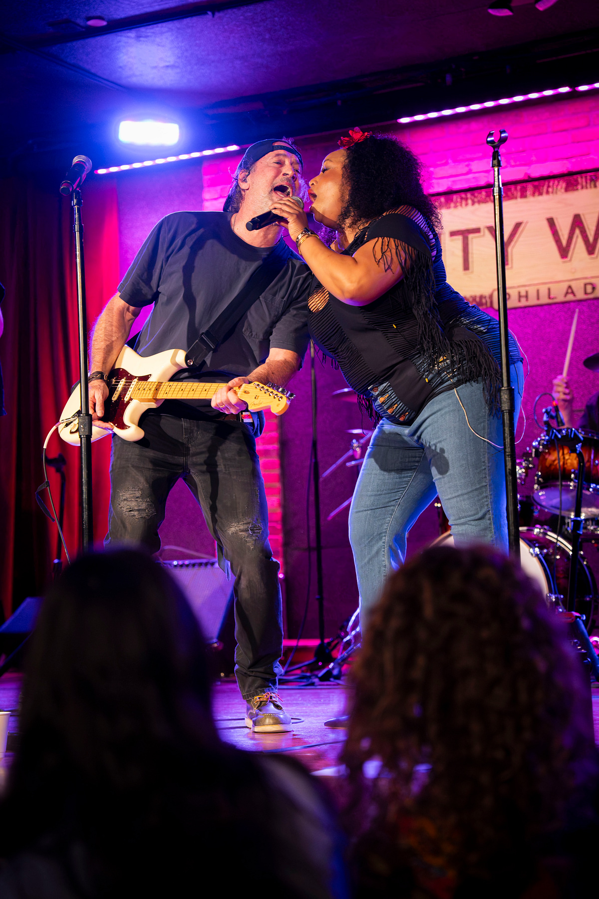 Two performers singing together on a brightly lit live event stage