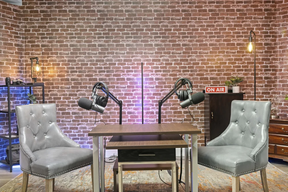 Two-seat podcast set photographed head-on against a lit brick wall