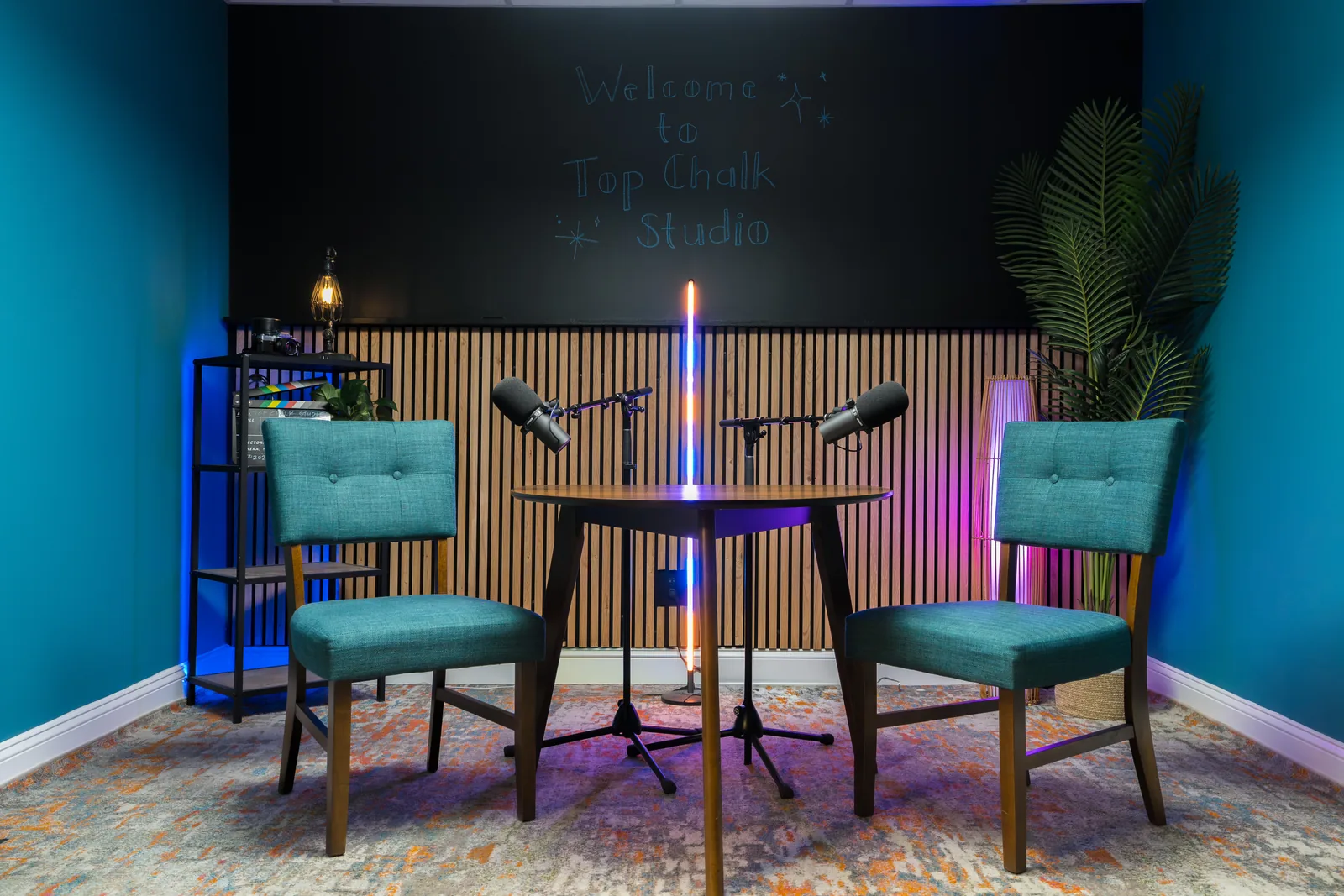 Podcast studio with three boom microphones over a round table, upholstered chairs and a slatted wood wall