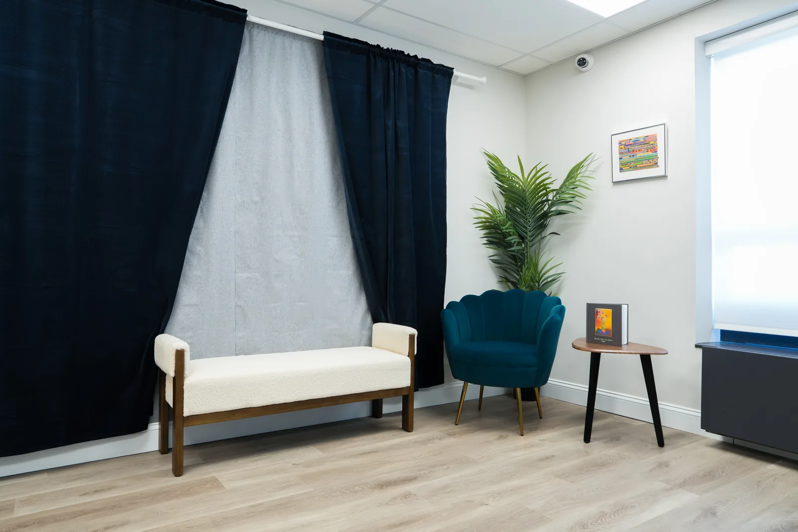 Portrait corner with a neutral backdrop, bench, accent chair and side table beside a window