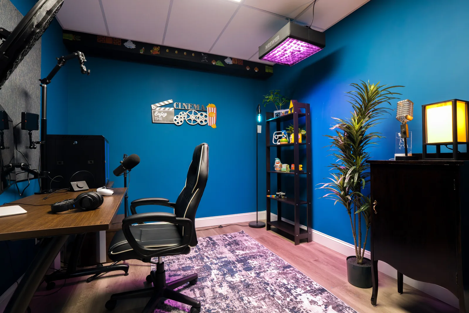 Streaming studio with a desk, microphone on a boom arm, chair and shelving against a deep blue wall